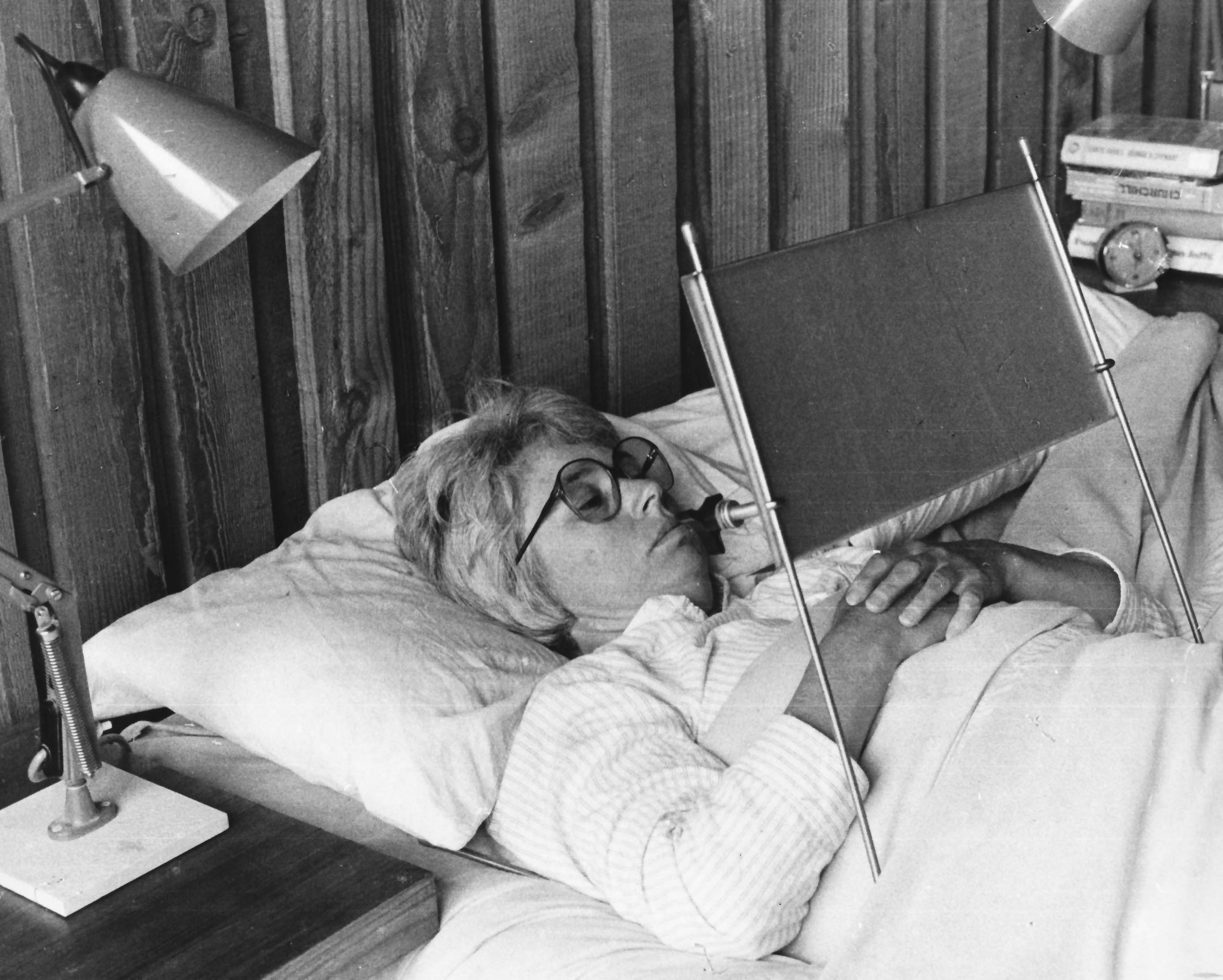 Maxine  reading a book lying down in bed with legs reversed. Also called Multi-purpose Reading Aid (MPRA)